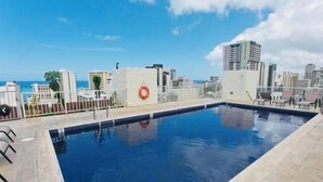 Una piscina al terrat amb un salvavides, envoltada d'edificis de la ciutat i un cel serè.