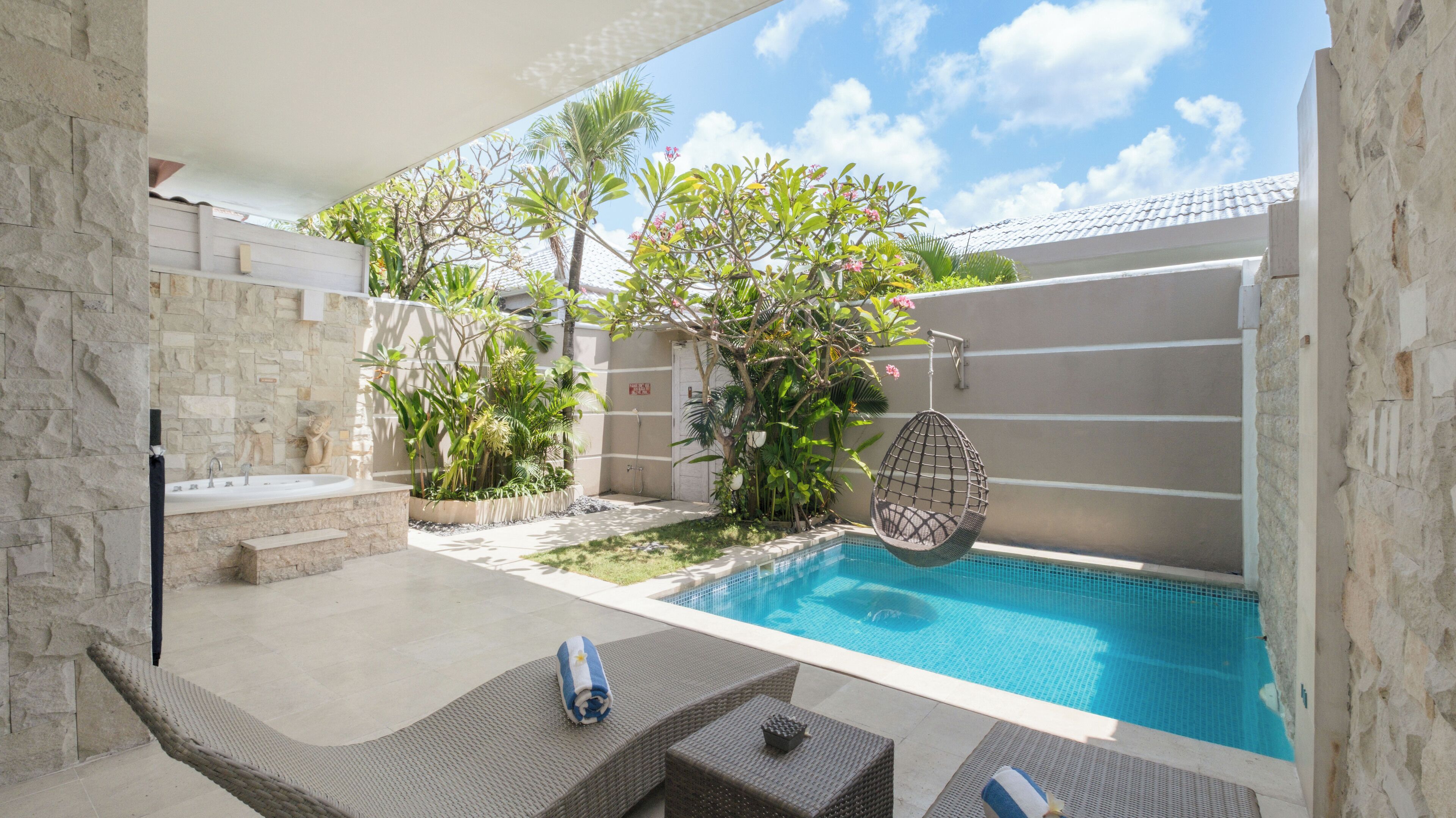 A poolside area with a stone wall, a hanging chair, and a small seating area with cushions.