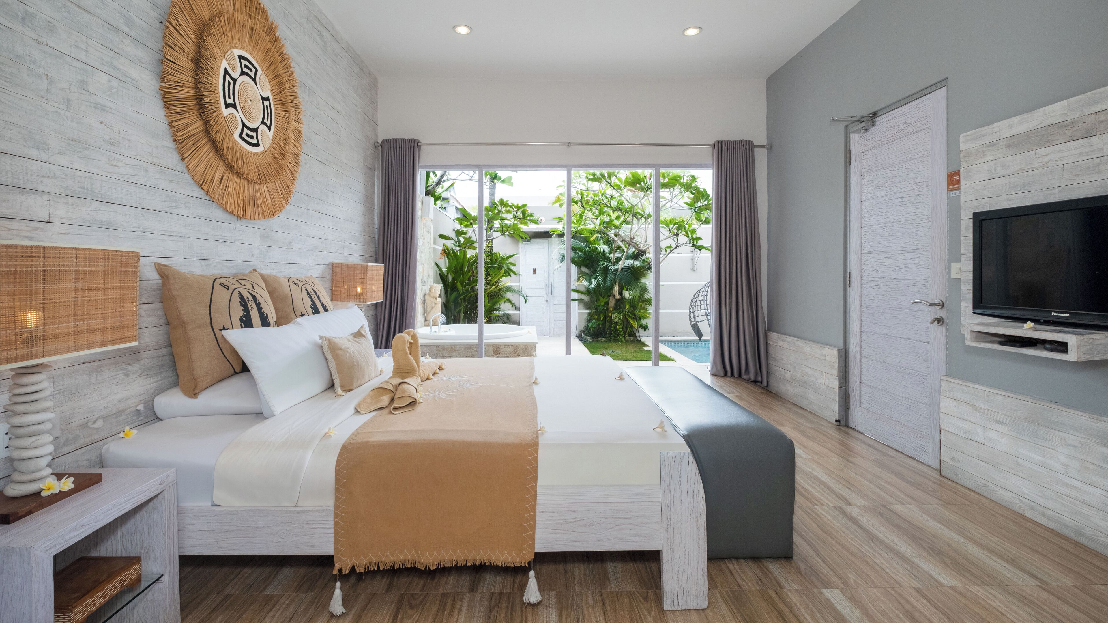 A modern bedroom with a large bed, a TV, and a view of a pool and greenery outside.