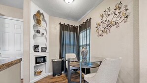 Un coin repas comprenant une table ronde, deux chaises, un élément décoratif mural et une fenêtre avec des rideaux.
