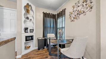A dining area with a round table, two chairs, a decorative wall piece, and a window with curtains.