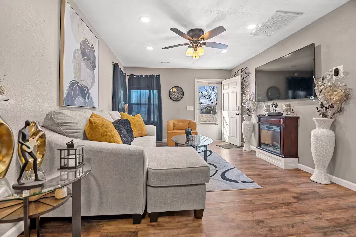 A modern living room with a grey sofa, yellow cushions, a glass coffee table, and a fireplace.
