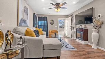 A modern living room with a grey sofa, yellow cushions, a glass coffee table, and a fireplace.
