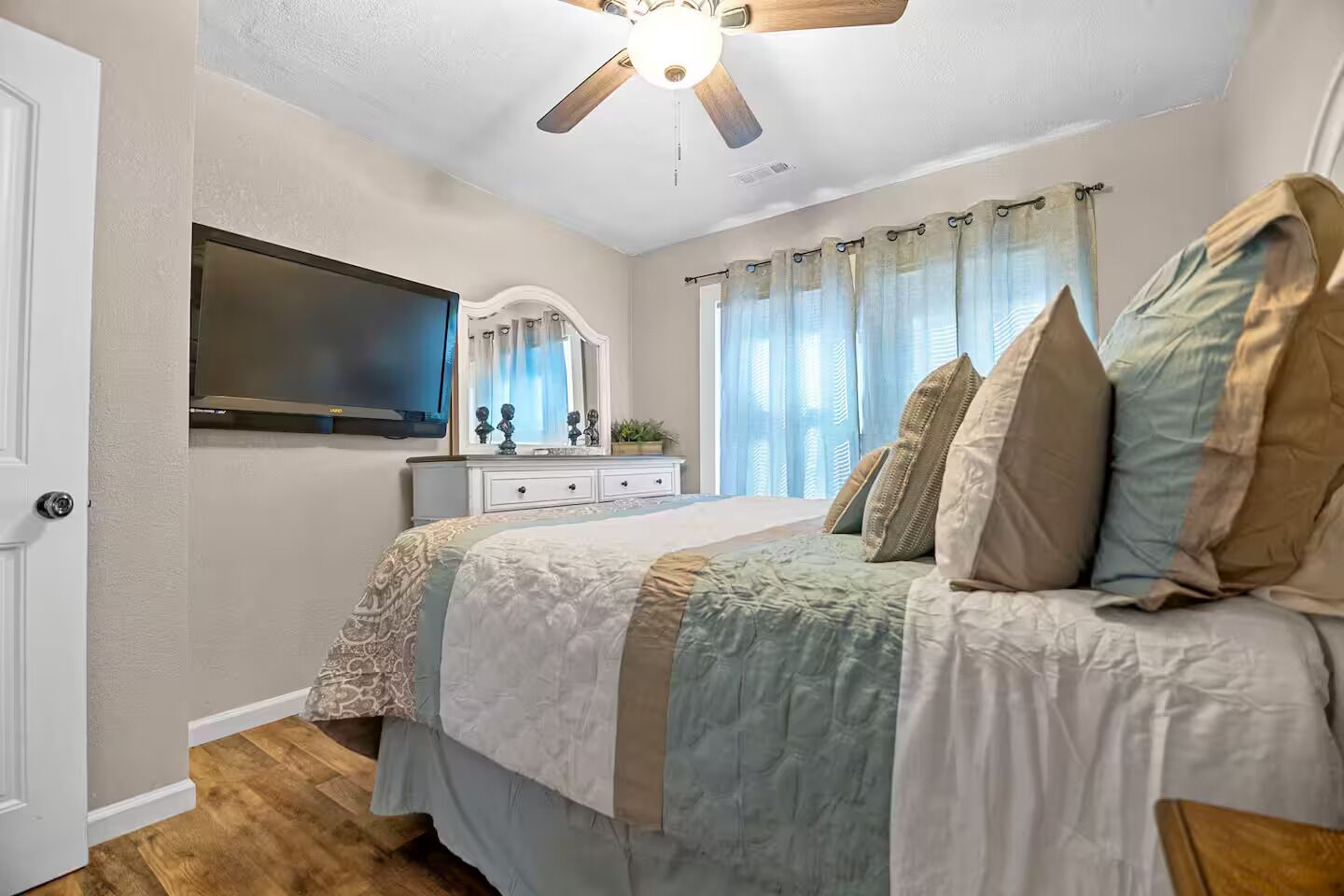 Une chambre à coucher avec un lit, une commode, un téléviseur et un ventilateur de plafond.