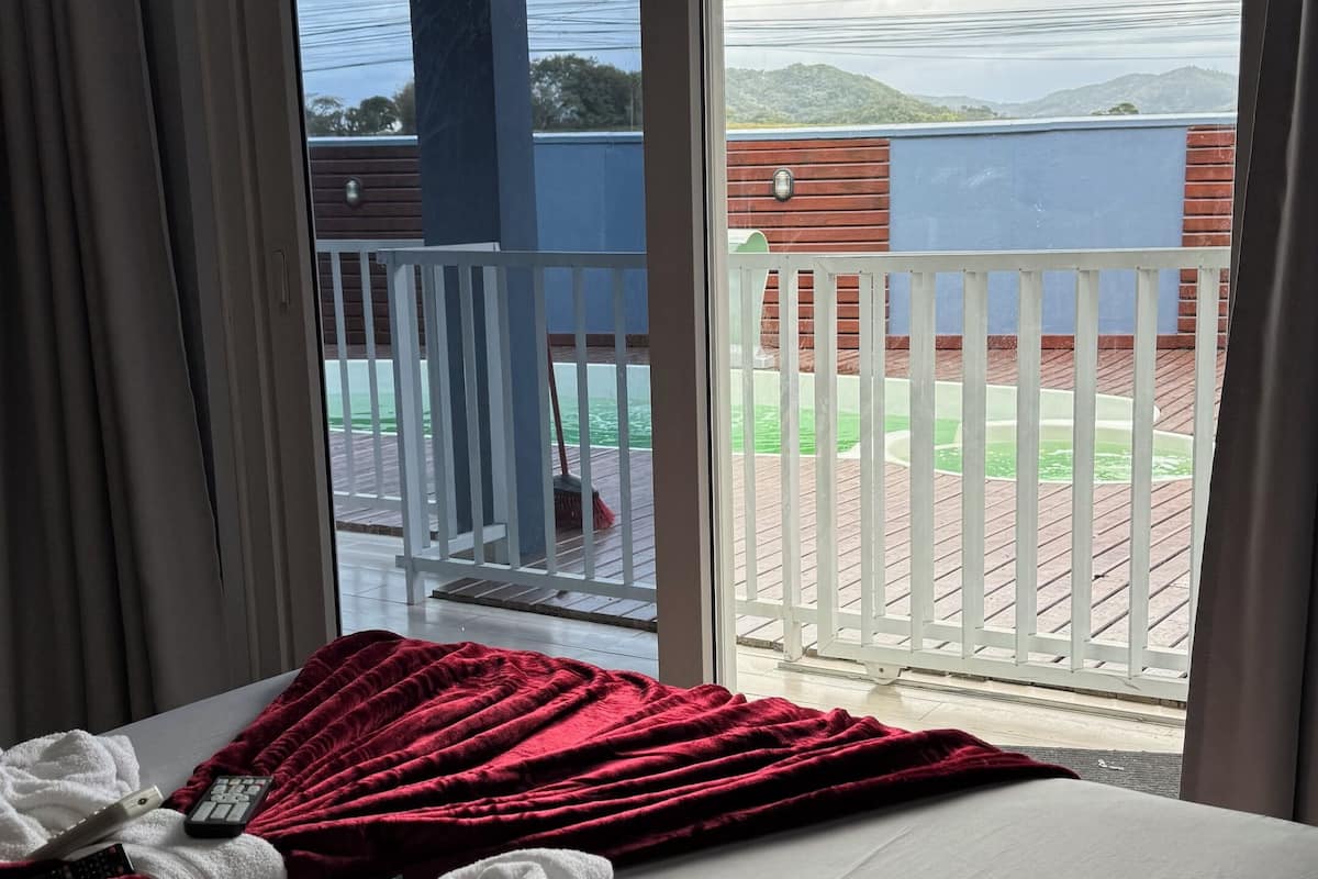 Quarto com uma cama, manta vermelha, toalhas brancas e um controle remoto.