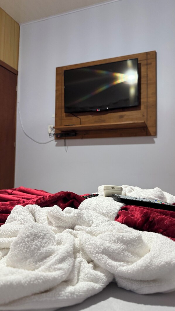 Un televisor montado en la pared sobre una cama con una colcha roja y blanca.