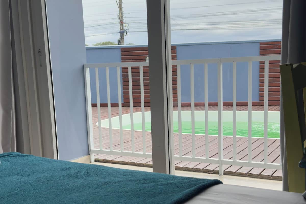 Quarto com cama, vista para uma varanda e piscina.