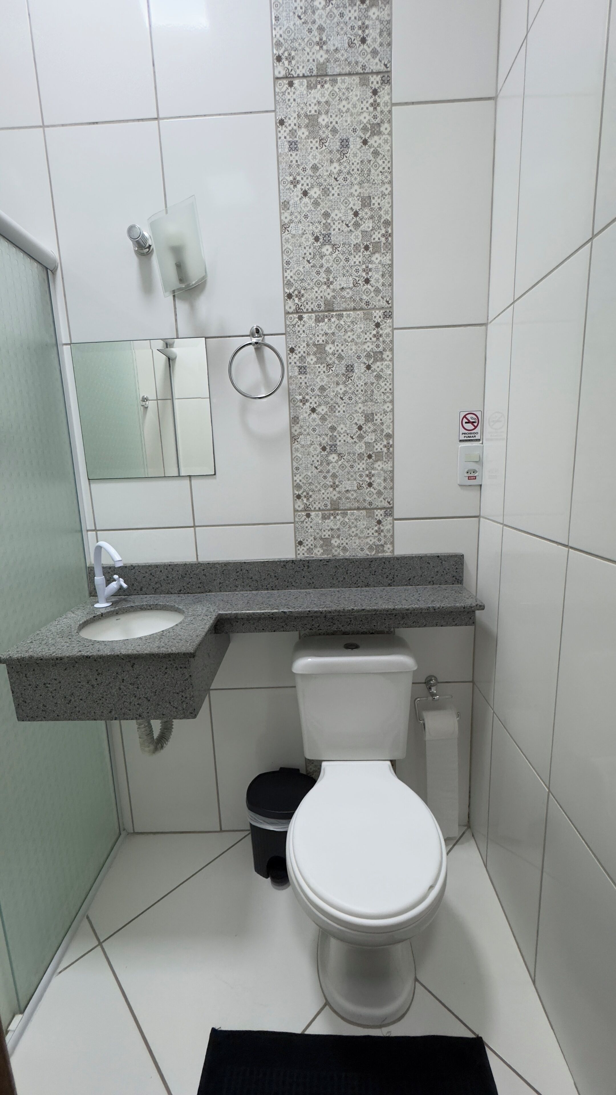 A compact bathroom with a white toilet, a sink with a granite countertop, a glass shower enclosure, and a patterned tile backsplash.