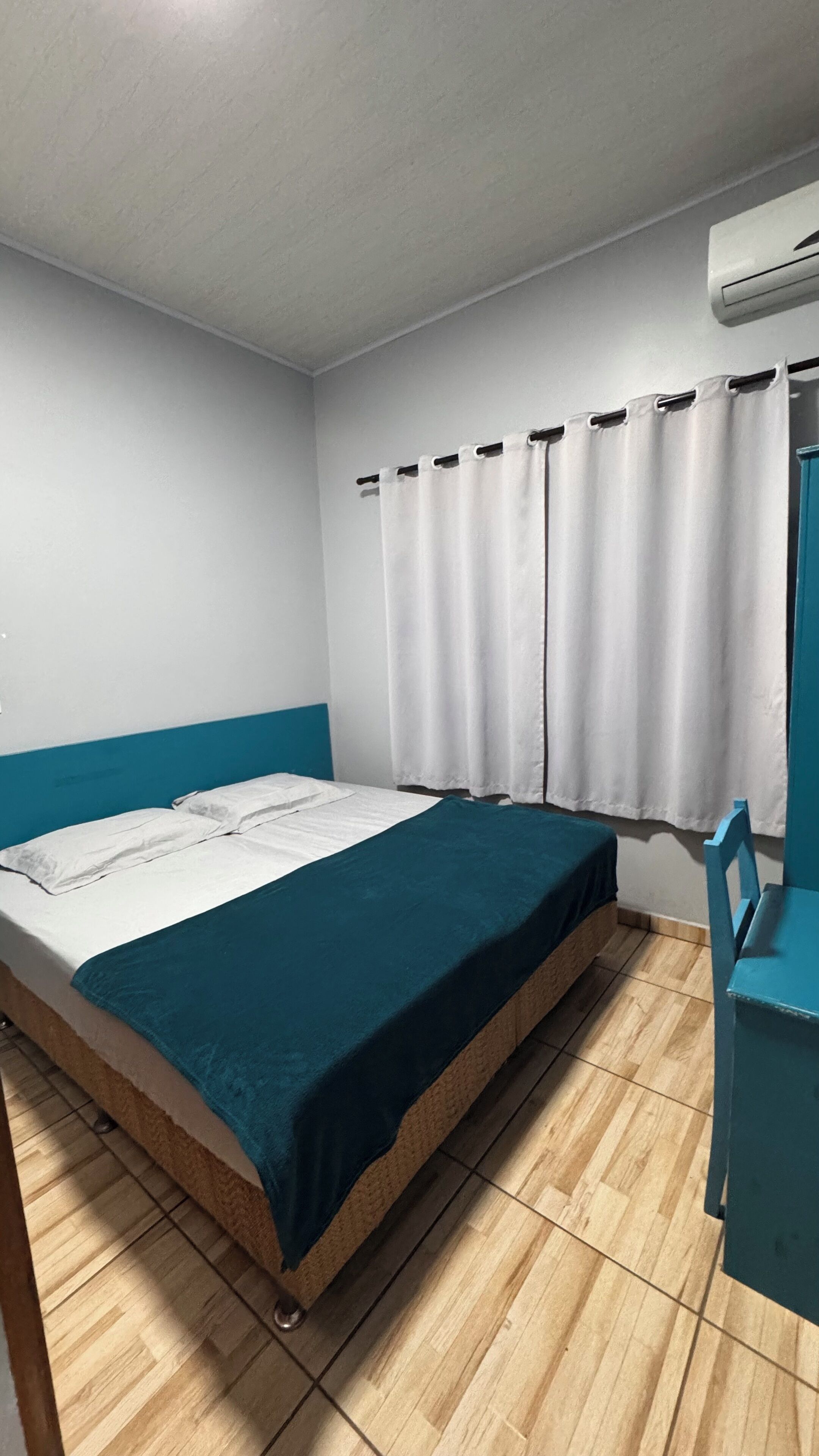 Ein Einzelbett mit türkisfarbener Bettdecke in einem Zimmer mit hellem Holzboden, weißen Wänden und einer blauen Akzentwand.