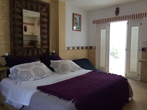 Quarto com cama grande, espelho, quadro e porta que dá para área externa.