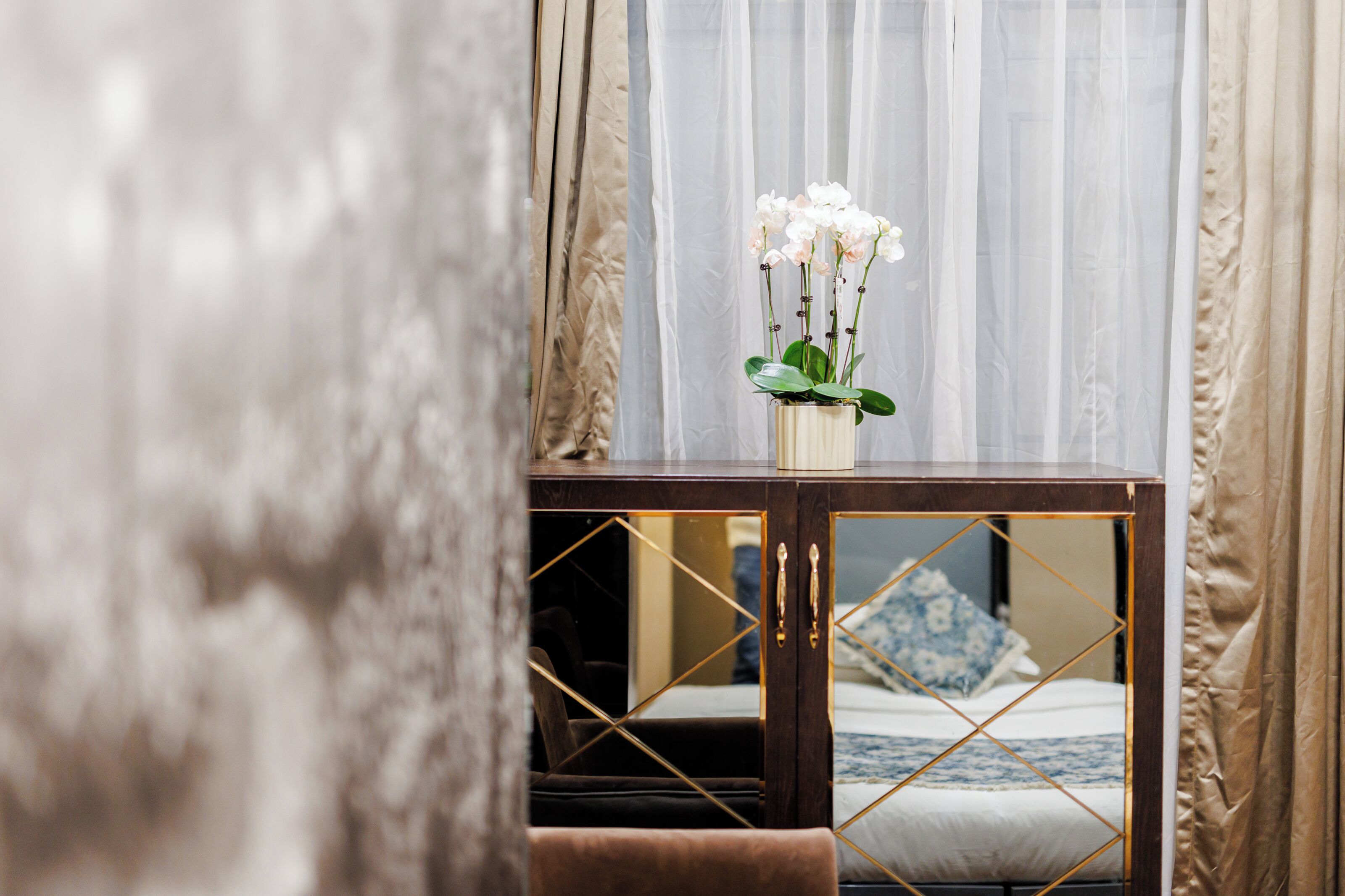 A bedroom with a bed, a bedside table with a vase of flowers, and sheer curtains.