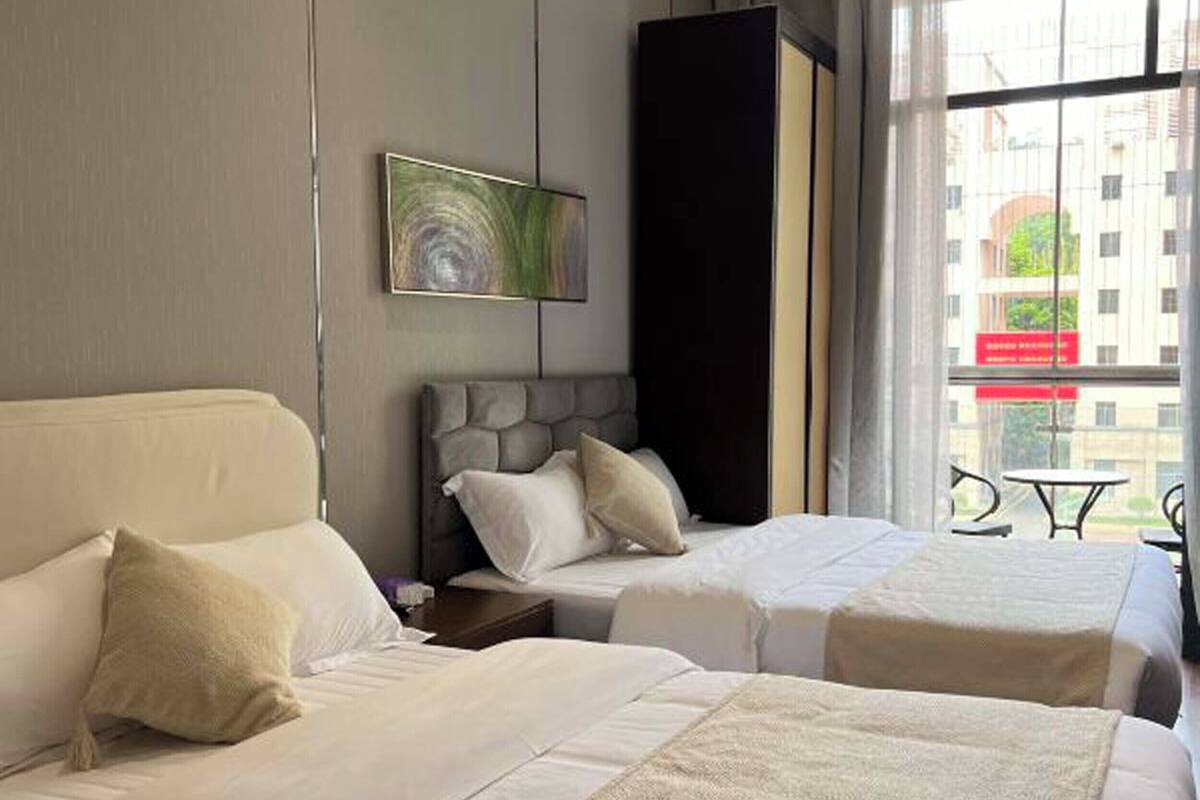 A hotel room with two beds, a large window, and a painting on the wall.