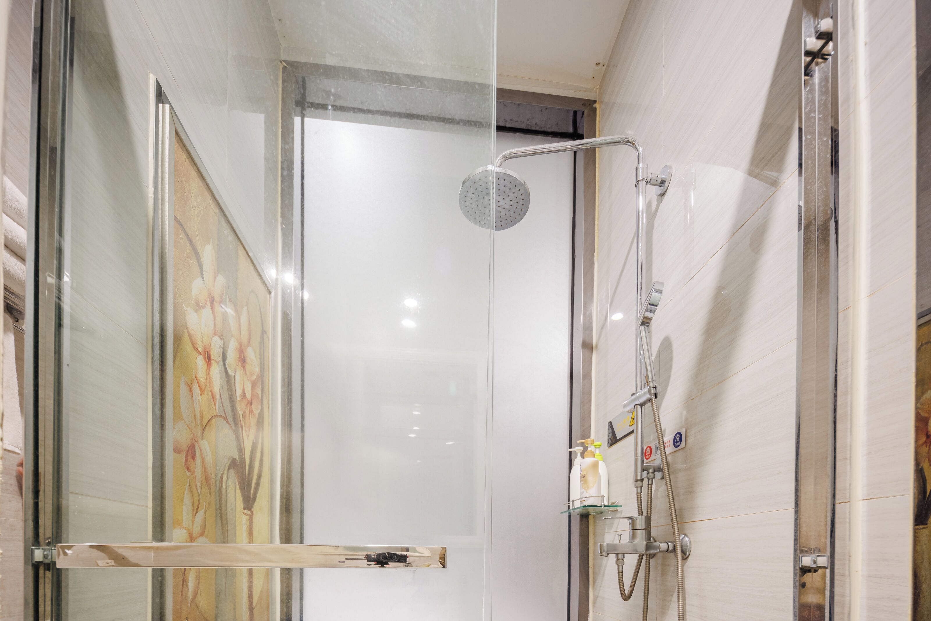 A glass-enclosed shower with a handheld showerhead and a wall-mounted faucet.
