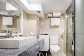 A modern bathroom with a marble countertop, a toilet, and a glass-enclosed shower.