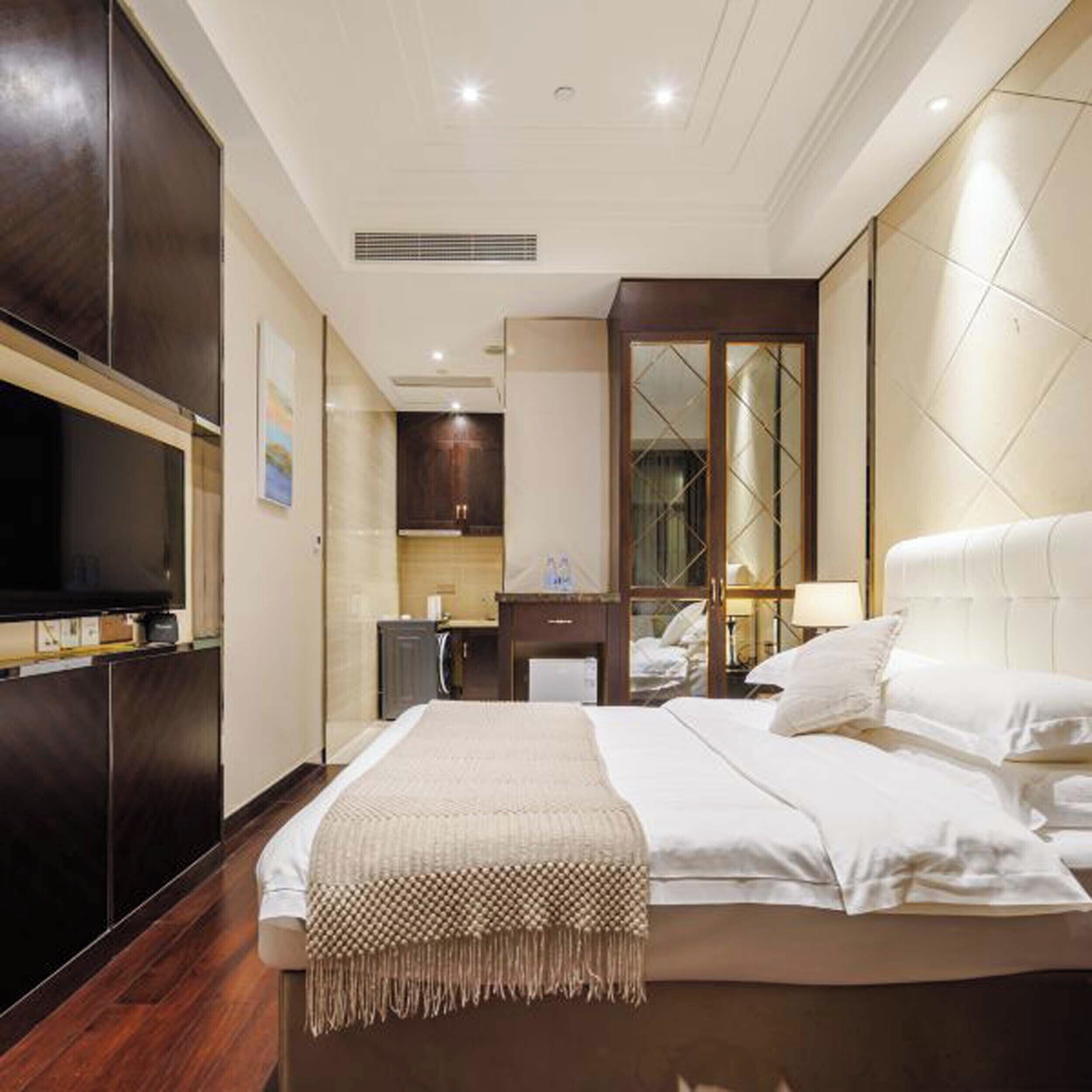A hotel room with a large bed, a TV mounted on the wall, a mirror, and a small kitchenette.