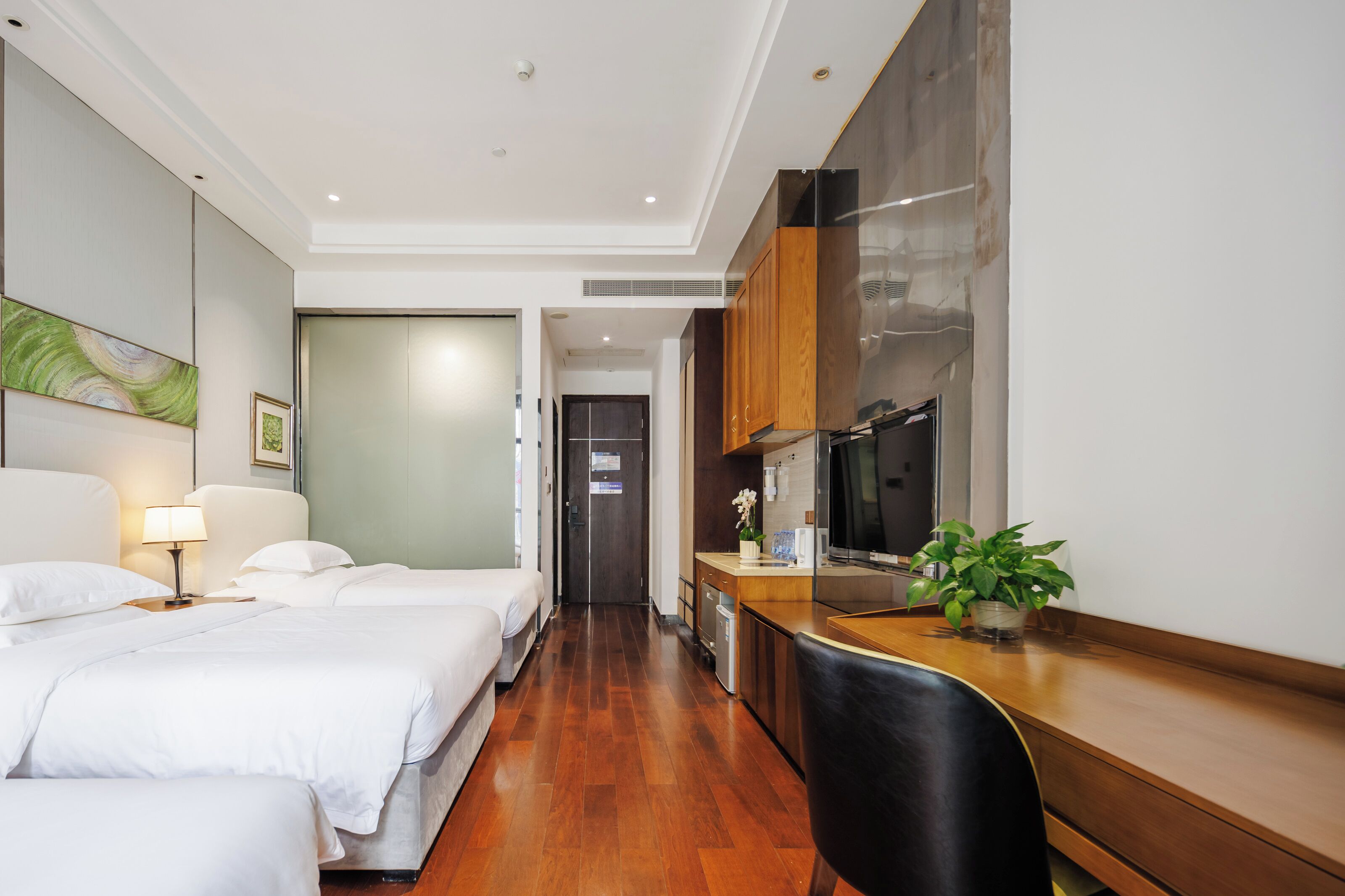Habitación de hotel con dos camas, un escritorio, un refrigerador y una planta en maceta.
