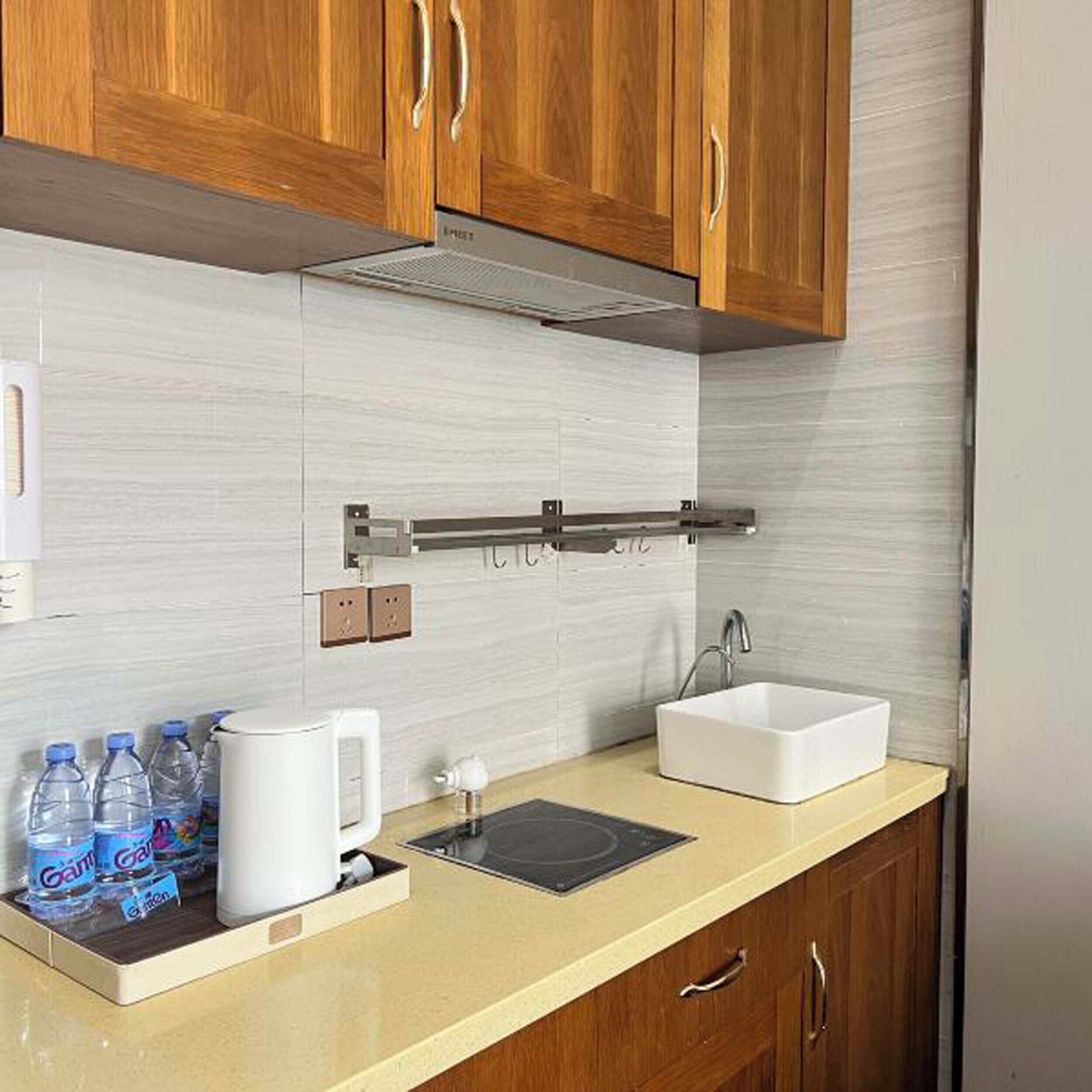 A kitchen with wooden cabinets, a white sink, and a countertop with a kettle and water bottles.