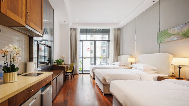 Une chambre d’hôtel avec une kitchenette, deux lits, un coin repas et une grande fenêtre avec des rideaux.