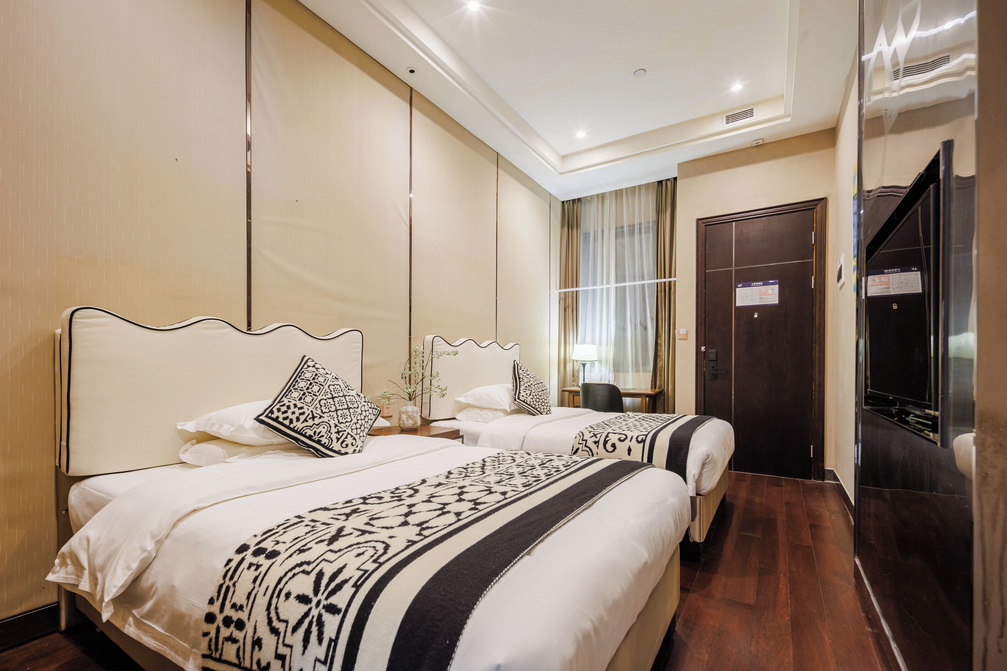A hotel room with two beds, a large mirror, a wardrobe, and a television.