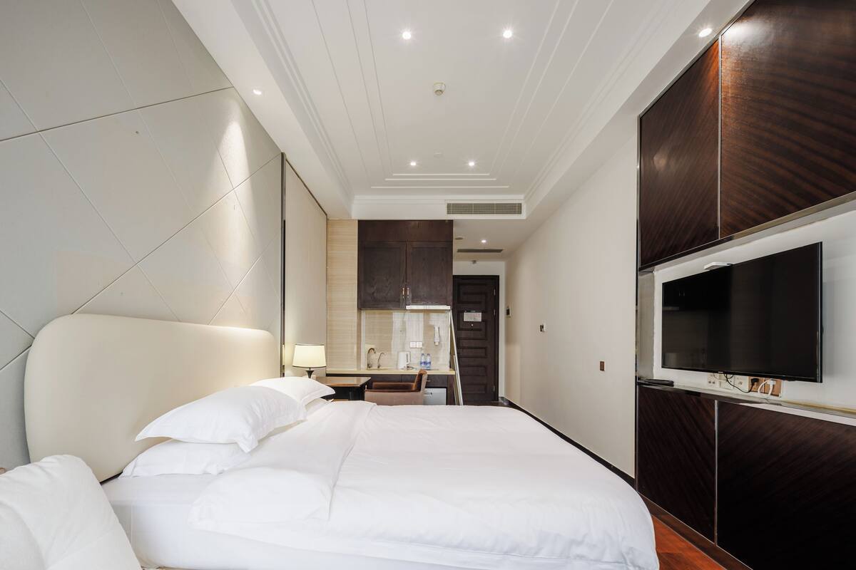 A modern hotel room with a large bed, a flat-screen TV, a desk with a chair, and a mirror.