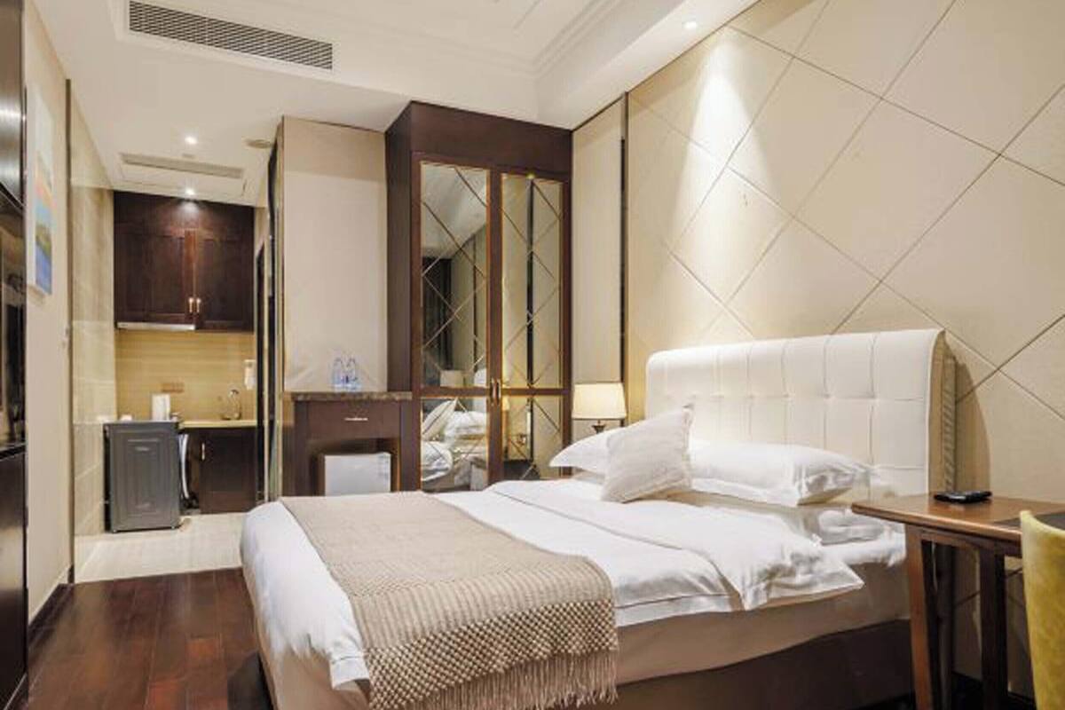 A hotel room with a large bed, a bedside table, a mirror, and a kitchenette area.