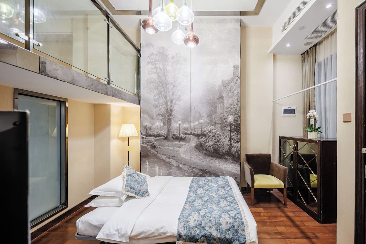 A modern hotel room with a large bed, a glass partition, a desk with a chair, and a wall-mounted air conditioner.