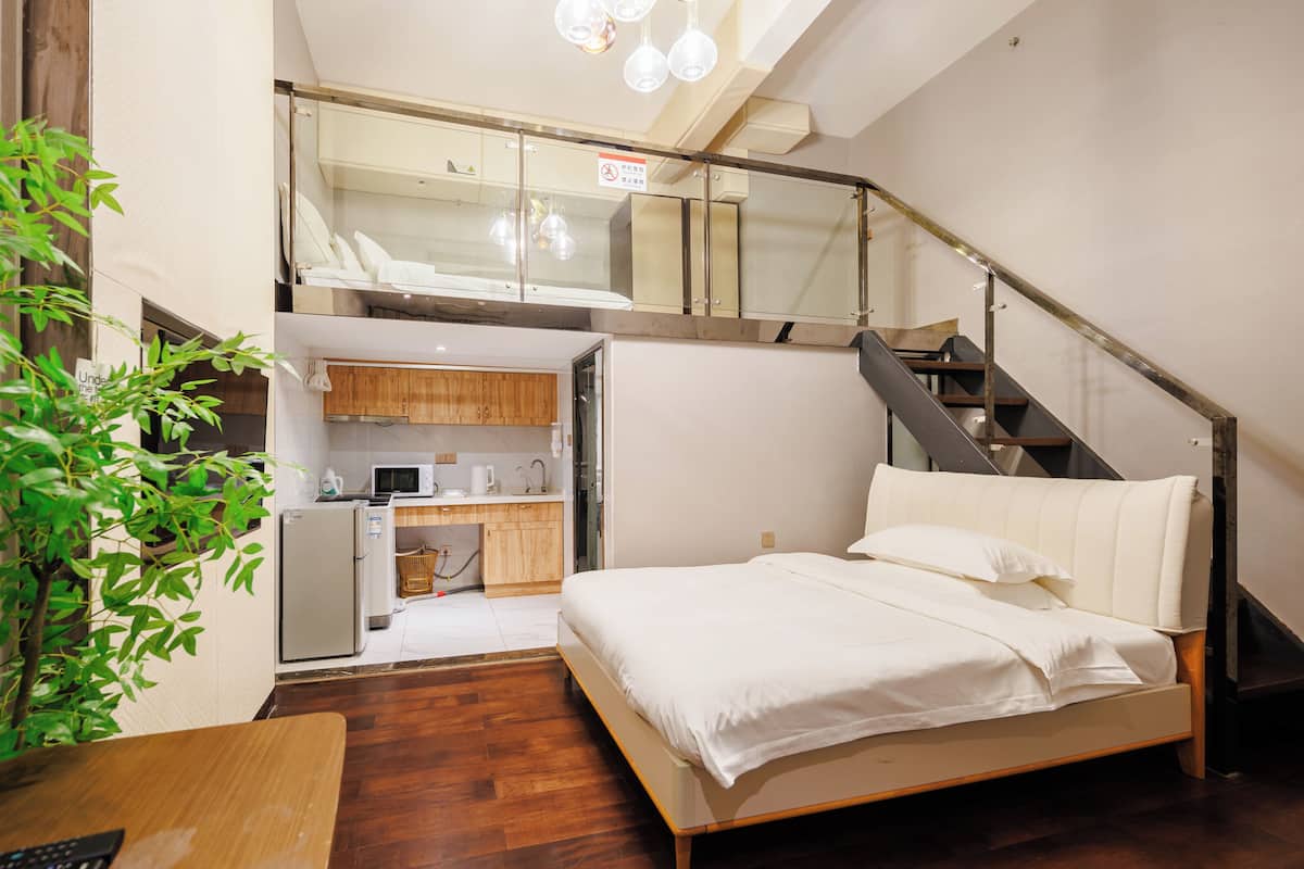 A compact bedroom with a bed, a small kitchenette, and a staircase leading to an upper level.
