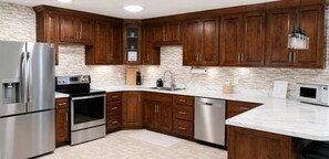 A kitchen with wooden cabinets, a stainless steel refrigerator, an oven, a dishwasher, and a marble countertop.