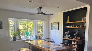 Ein Holzesstisch mit Bänken, Deckenventilator und eine Kaffeestation mit Regalen.