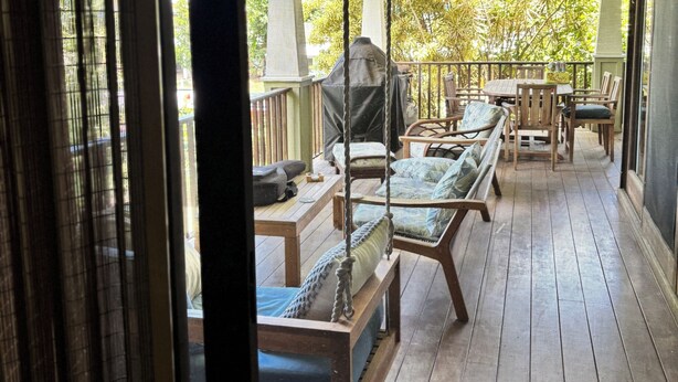 Ein überdachter Außenbereich mit Holzmöbeln, einem Deckenventilator und Blick auf Grünflächen.