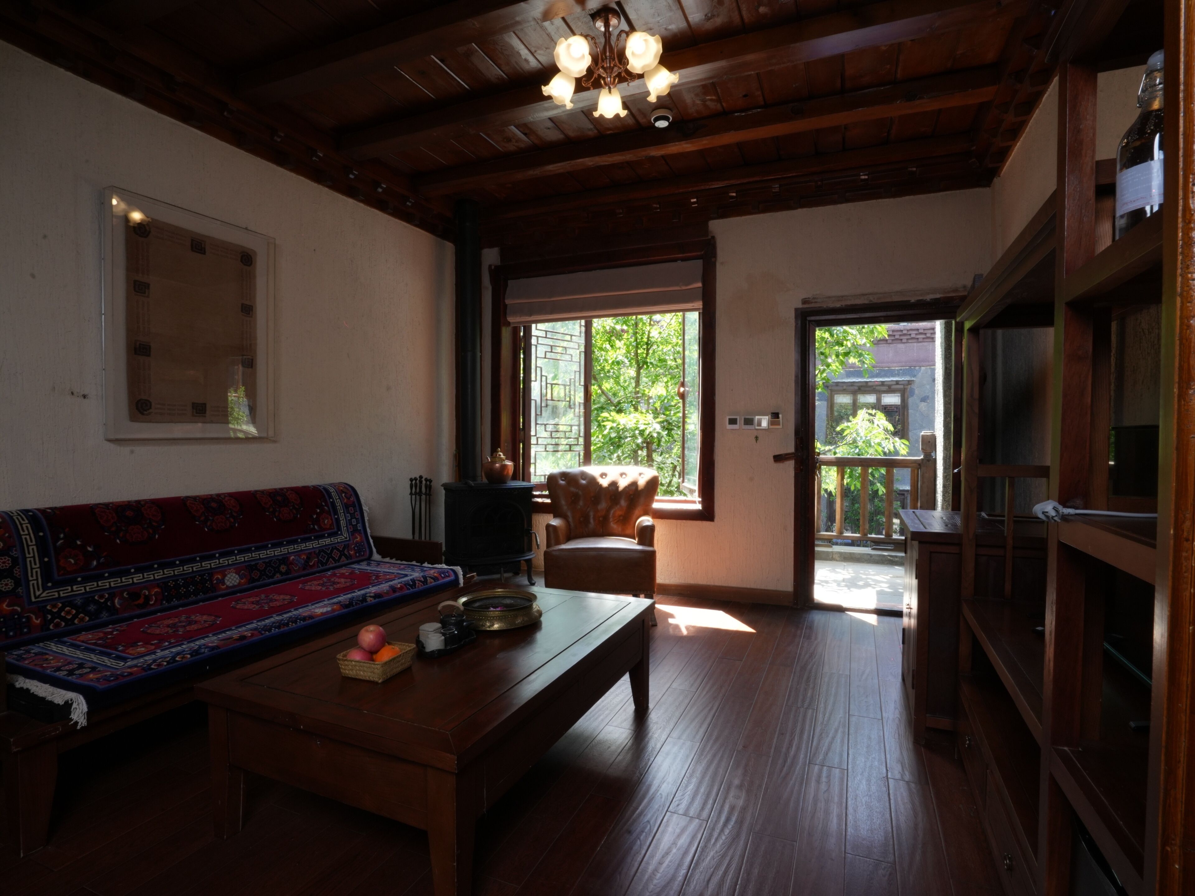 Una habitación tradicional con techo de madera, un sofá con funda estampada, una mesa de madera con cesta de frutas y vista a un jardín por la ventana.