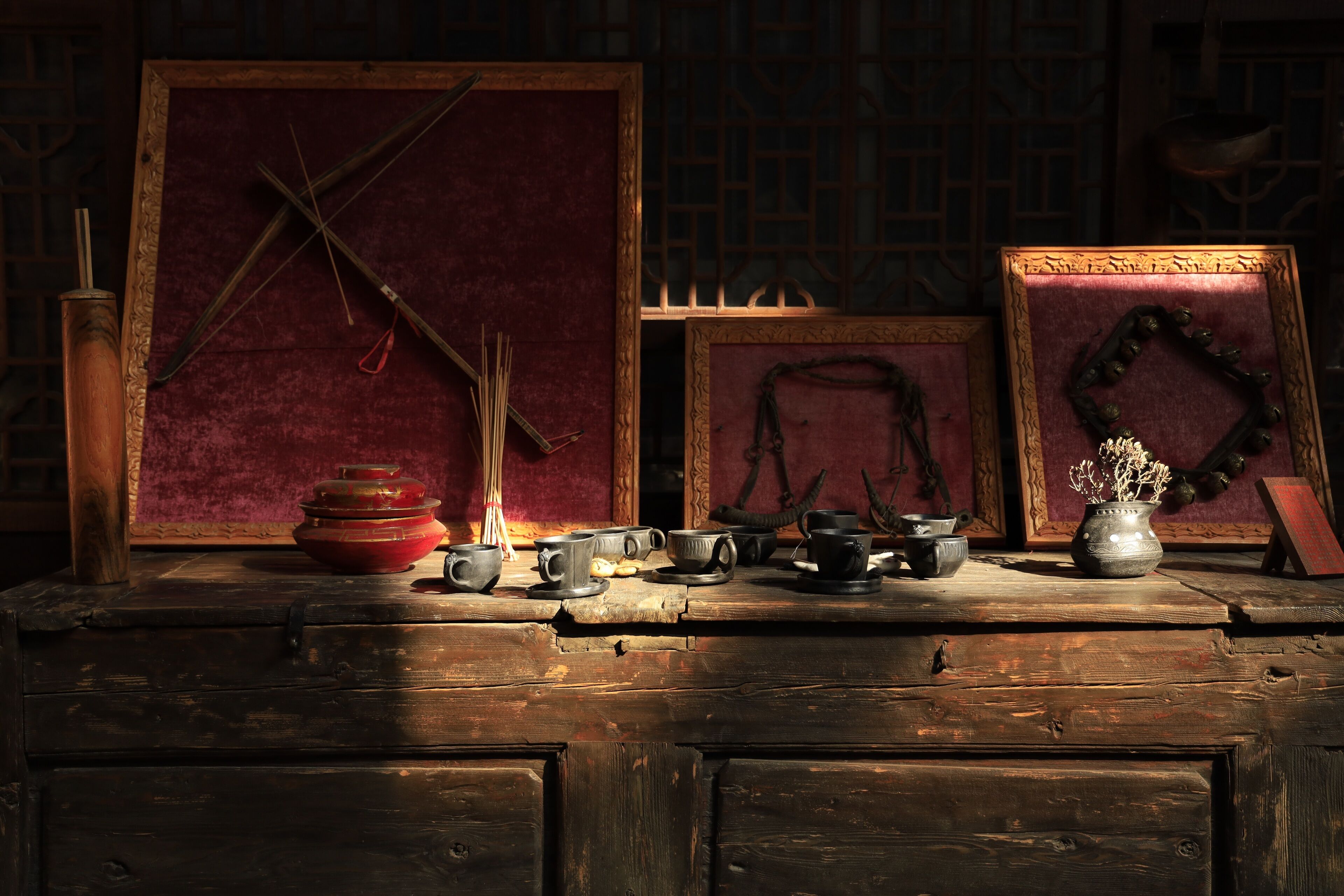 A wooden table with various items including a red bowl, cups, and a vase with dried plants.