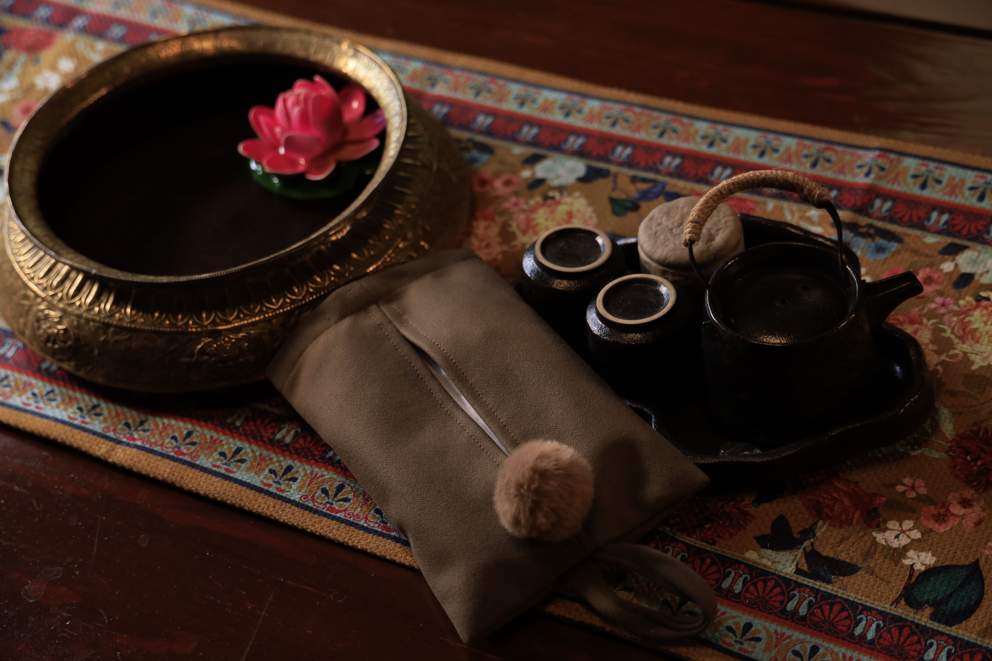Un juego de té tradicional con tetera, tazas y un cuenco decorativo con una flor rosa.