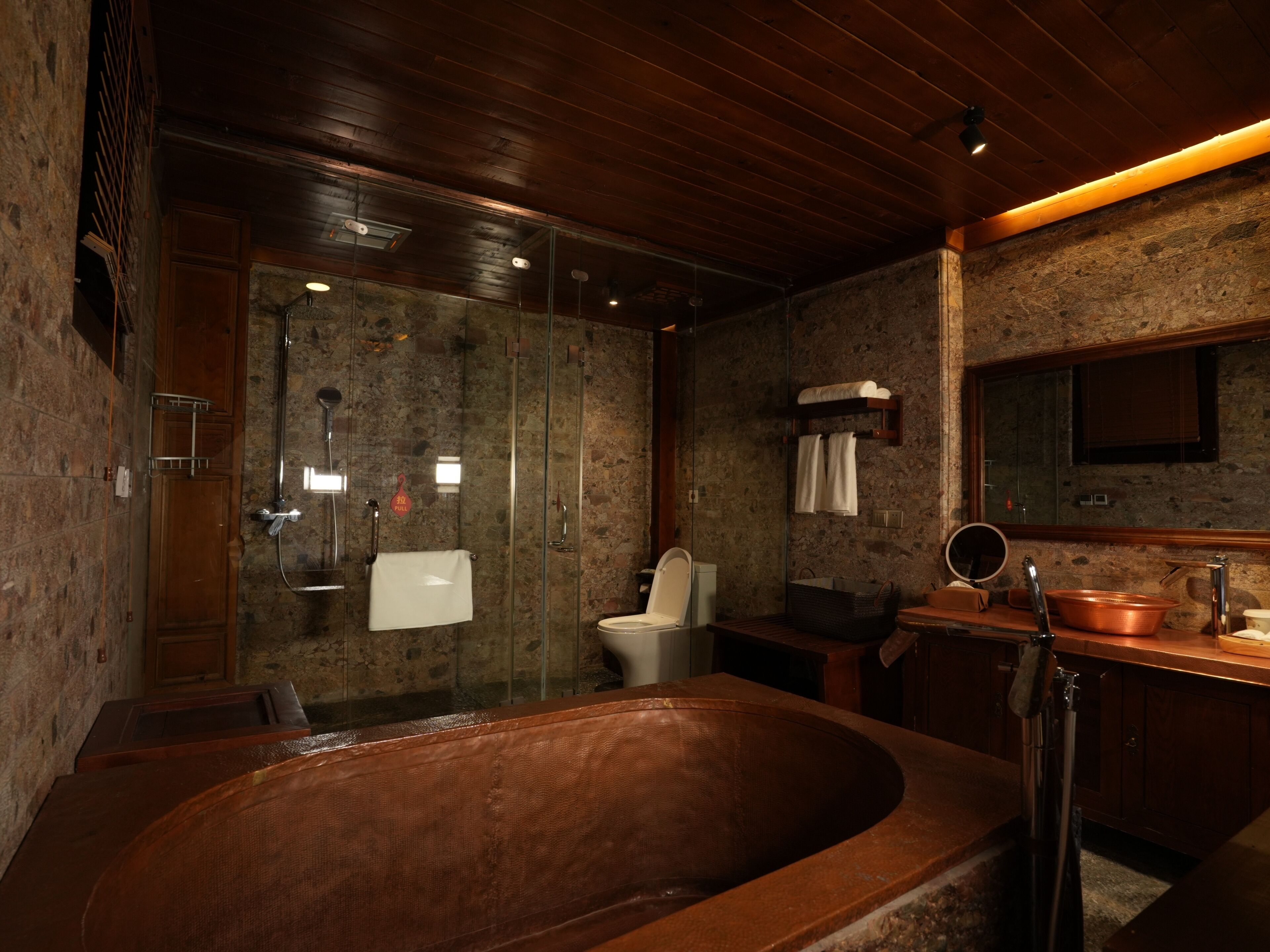 A modern bathroom with a large bathtub, a glass-enclosed shower, and a wooden vanity with a copper basin.