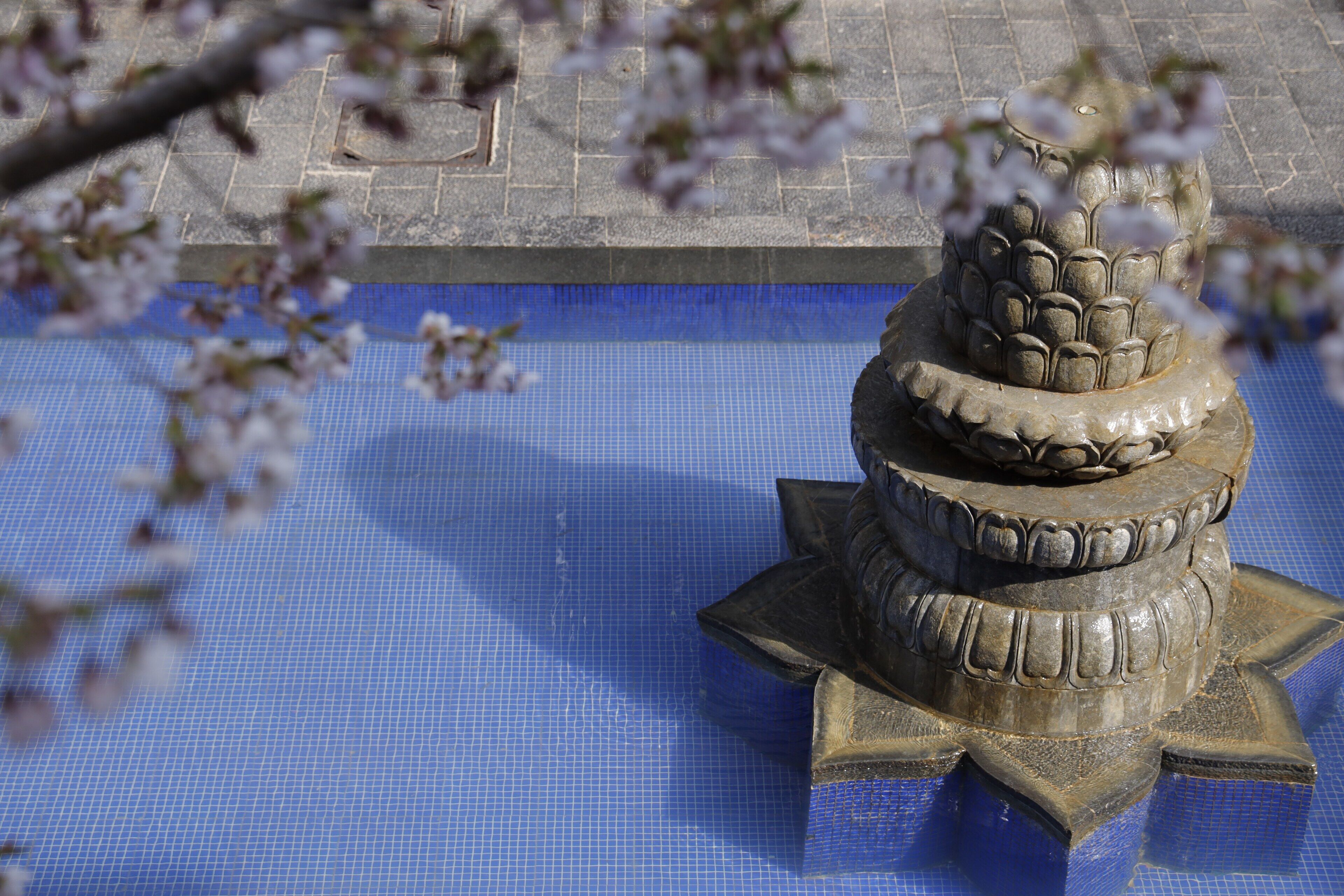 A stone fountain with a tiered design, surrounded by a blue tiled area.