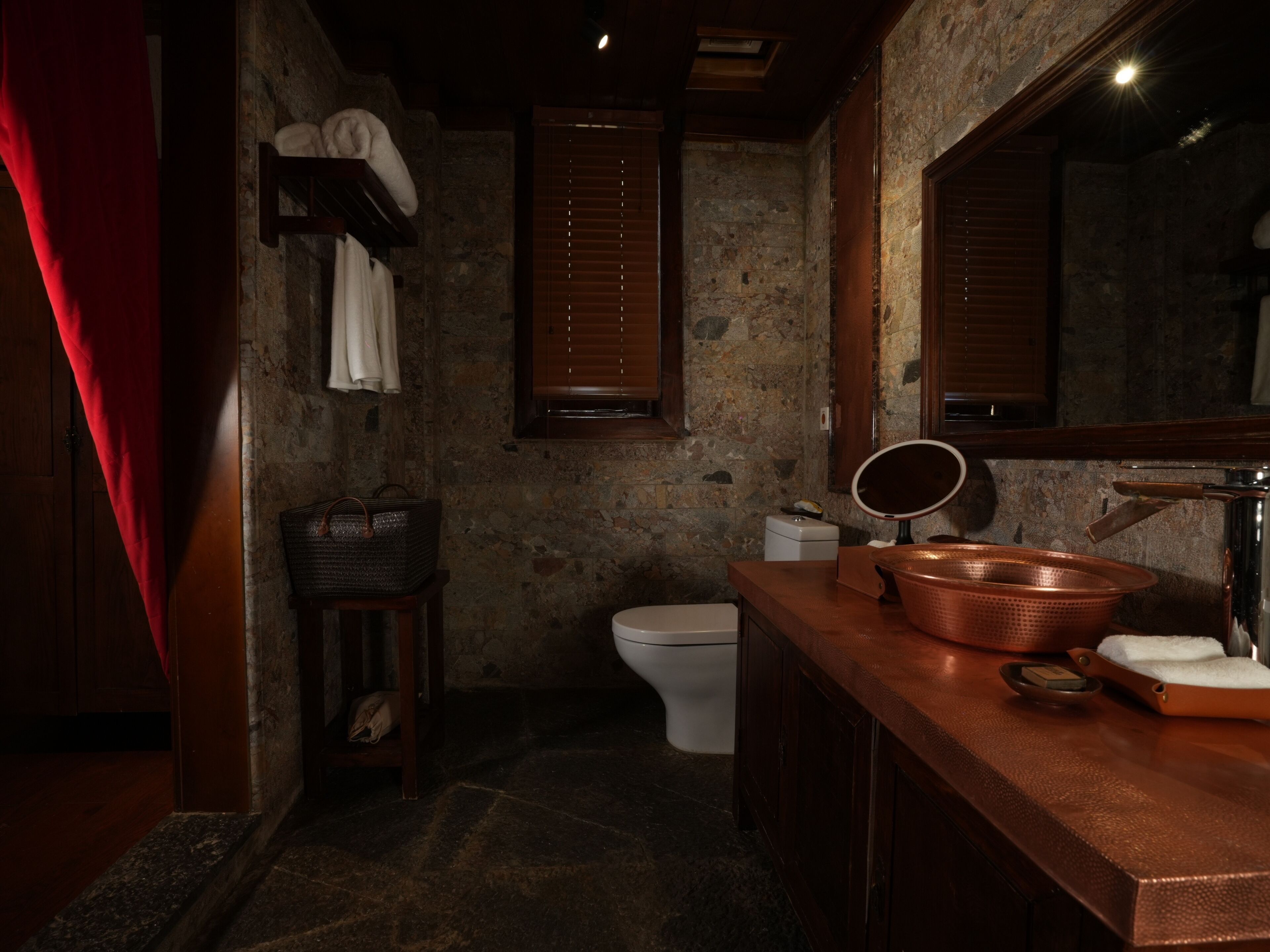 A rustic bathroom with a stone wall, wooden vanity, and a white toilet.
