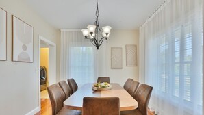 A dining room with a round table, six chairs, a chandelier, and a fruit bowl.