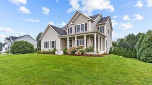 A two-story house with a front porch, a well-maintained lawn, and a large garden with flowers.