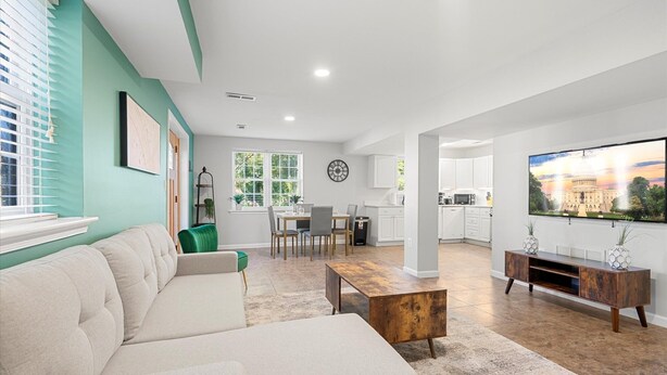 A modern living room with a sectional sofa, a coffee table, and a dining area with chairs and a table. - The Jefferson | Emerald | City View (Alexandria)