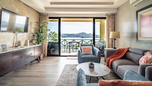 Una sala de estar moderna con un televisor grande, asientos cómodos, una mesa de centro y vistas a una montaña y al agua.