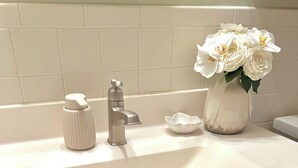 Un lavabo de salle de bain doté d’un robinet moderne, d’un distributeur de savon, d’un petit bol blanc et d’un vase contenant des fleurs blanches.