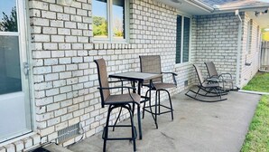A house with a brick exterior, a covered patio with a table and chairs, and a rocking chair. - Sunlit Maple Inn-Rest Awaits You (Hutchinson)