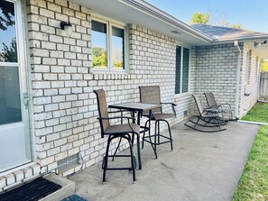 Ein Haus mit Ziegelhausfassade, einer überdachten Terrasse mit Tisch und Stühlen sowie einem Schaukelstuhl.