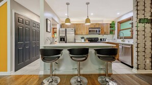 A modern kitchen with a central island, bar stools, wooden cabinets, stainless steel appliances, and pendant lighting. - Secluded Cabin Oasis Located in North Raleigh... (Raleigh)