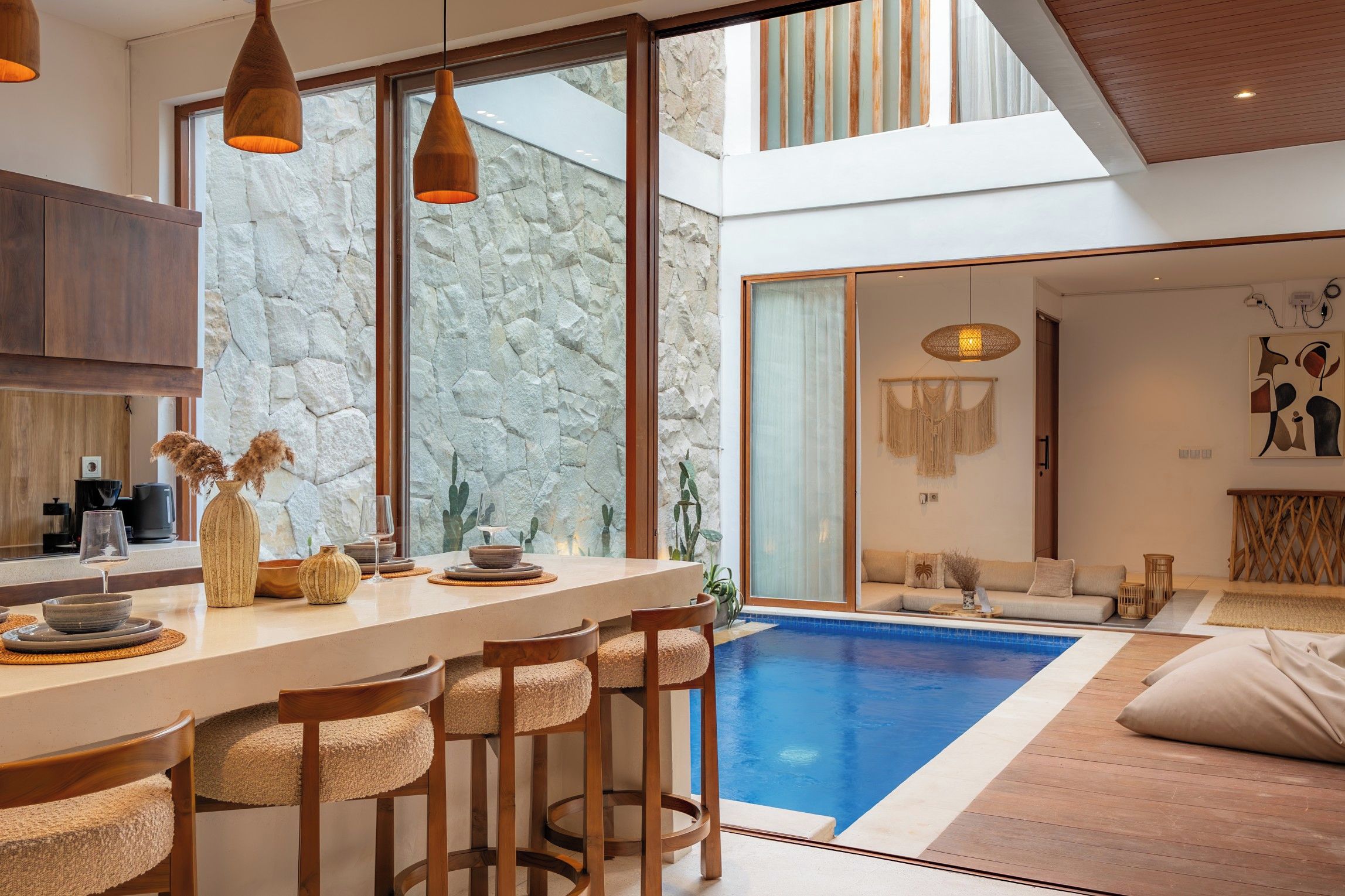 Une cuisine moderne avec un mur en pierre, un coin repas avec des tabourets de bar et une piscine.