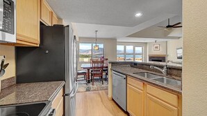 A kitchen with granite countertops, wooden cabinets, a black refrigerator, and a view of the mountains through large windows. - Stunning Vista at Alpine Buzz (Frisco)
