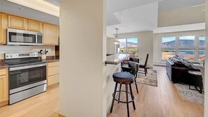 A modern kitchen with built-in appliances, a dining area with bar stools, and a view of a mountainous landscape through large windows. - Stunning Vista at Alpine Buzz (Frisco)