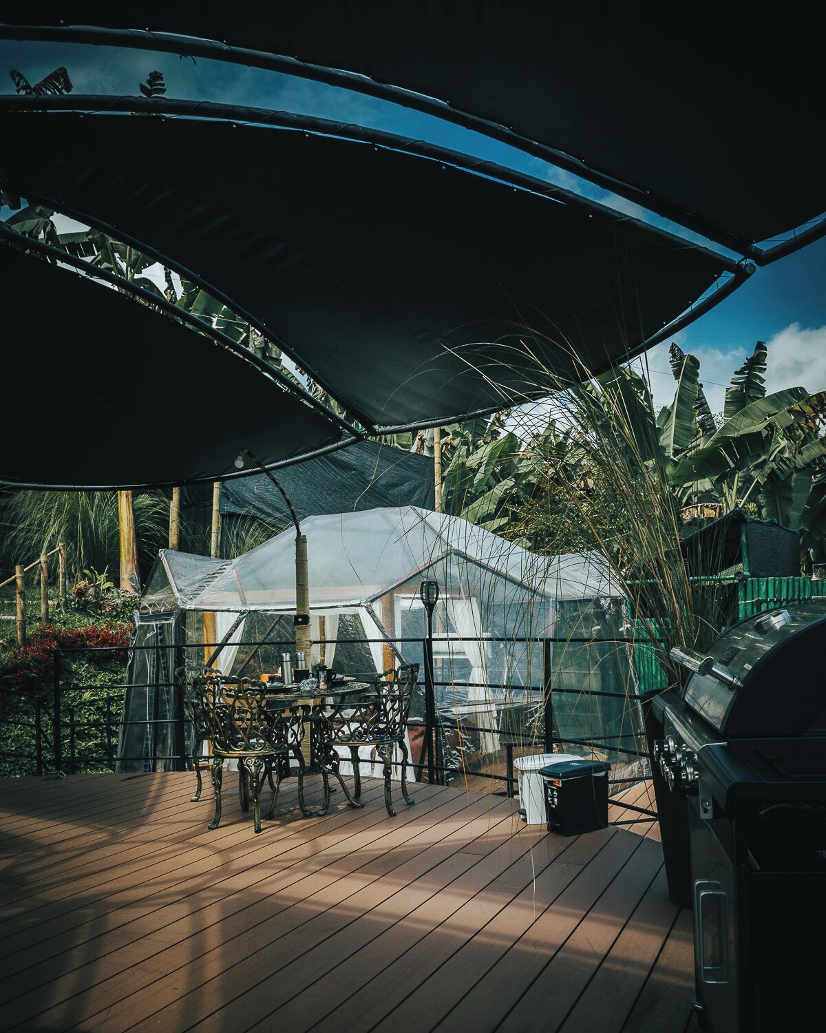 A covered outdoor area with a table and chairs, a grill, and a greenhouse structure.