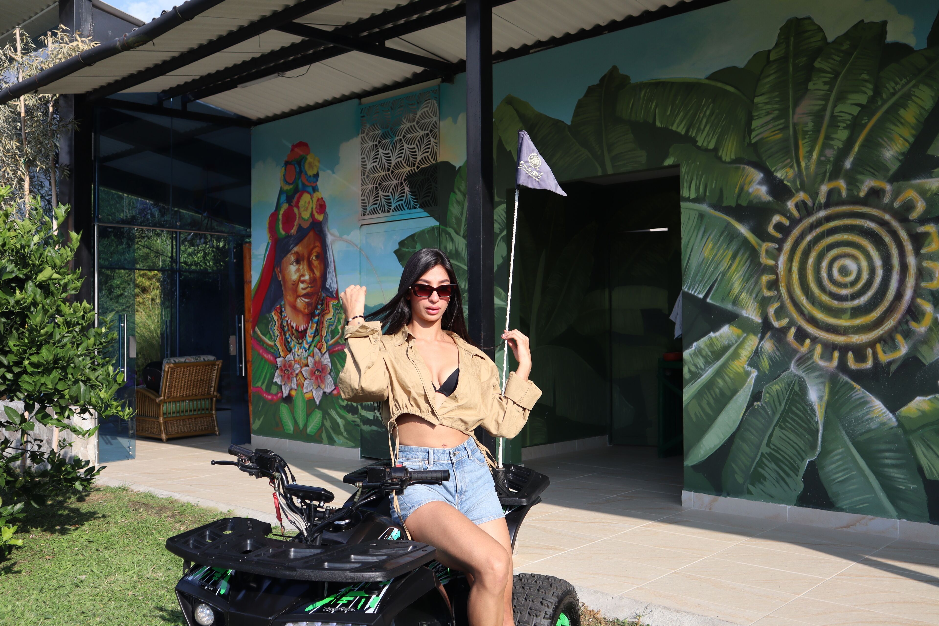 A person on an ATV in front of a building with a mural of a woman and a large leaf.