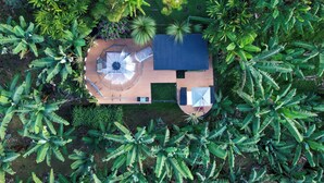 An aerial view of a garden with a wooden deck, a central table with chairs, and surrounding lush vegetation. - Chamí Glamping (Manizales)